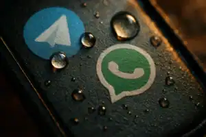 Логотипи Telegram і WhatsApp на поверхні, покритій краплями води.