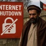 Man with beard stands next to an "Internet Shutdown" sign in Afghanistan.