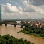Cityscape featuring a bridge, river, and modern skyscraper under cloudy skies.