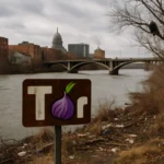 Schild mit 'Tor' und Zwiebel-Symbol am Flussufer unter bewölktem Himmel.