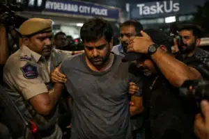 Individual in distress being escorted by police under bright lights.