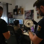 Two officers investigate a computer setup in a room, examining a clock.